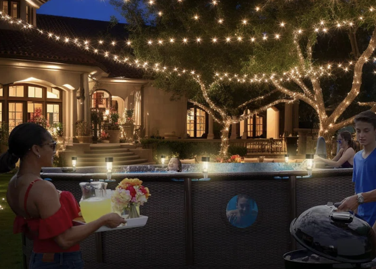 An above-ground pool with lights on it's gutter area and string lights hanging above.